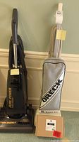 Photo showing Sharp Twin Energy upright vacuum with hose, and Oreck XL vacuum with carrying bag and a small brown box of accessories in front.