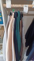Side view of multiple women's clothing items on hangers in neutral tones including pastel cream, green, gray, and navy, to show the quantity and variety.