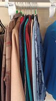 Photo showing seven women's clothing items hanging on a rack including coats and sweaters in various colors.