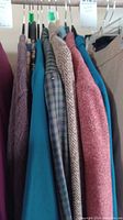 Side view of six women's jackets on hangers in colors including maroon, beige houndstooth, teal, and dark reddish with textured fabrics