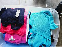 Overall view of folded women's sweaters and tops in various colors in a plastic storage bin