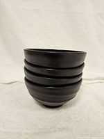 Stack of four black melamine bowls showing smooth rounded exterior and height.