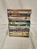 Stack of 17 adult comedy DVDs showing spines and part covers in a pile on a light colored fabric surface.