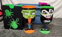 Two Halloween-themed drinking goblets depicting Frankenstein and a vampire characters, made of painted material with colorful stands.