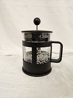 Glass and black Bodum French press coffee maker with plunger and handle, featuring decorative swirls on glass body.
