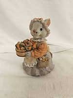 Front view of bunny piggy bank figurine dressed in bonnet, orange blouse, and gray skirt holding a basket of carrots with another basket hanging on the arm.