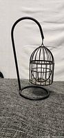 Metal hanging candle holder with a curved stand and hanging cage for candle.