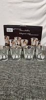 Six vintage glass candle holders with silver gilded holiday patterns displayed in front of original packaging box.