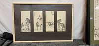 Framed artwork showing four vertical ink painting panels of horses with beige frame and dark matting