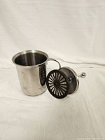 Side view of the stainless steel creamer container with handle and separate frothing plunger beside it.