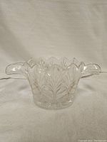 Clear glass bowl with leaf pattern engraved around sides and base, showing scalloped rim and two handles.