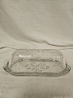 Full view of glass butter dish with cover on base showing floral etched pattern and small handles on the base.