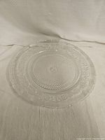 Full view of round glass plate showing overall embossed decorative pattern and textured center.