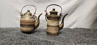 Front view of two decorative teapots made from granite and brass materials on a textured gray surface