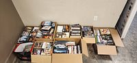 Multiple cardboard boxes and a tote bag filled with DVDs lined up on floor.