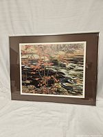 Frontal photo of the framed artwork showing creek, flowing water, rocks, and orange leaves on trees.