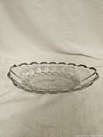 Angle view of the clear oval glass dish showing scalloped edge and starburst pattern at the base.