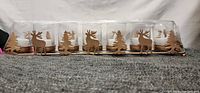 Row of 7 clear glass tealight holders with gold bases featuring reindeer and pine tree cut-out designs
