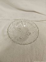 Top-down view showing the inner pattern and scalloped edge of the clear glass bowl on a white textured cloth.
