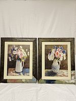 Front view photo showing both framed floral paintings side by side with painted frames and cream matting.