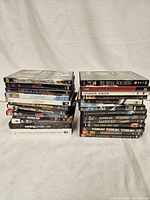 Photo showing front and spine of 16 DVDs stacked in two vertical piles on a white fabric background.