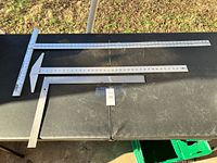 Three metal T-squares of different sizes placed on a table outdoors, showing full length and measurements.