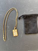 Necklace with rectangular pendant laid flat beside black velvet pouch on a dark surface