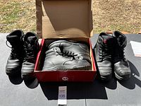 Photo of two pairs of black work boots outdoors, one pair in a red box, showing overall condition and colors.