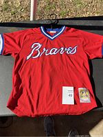 Full front view of red Atlanta Braves replica baseball jersey laying flat showing 'Braves' logo and tag with lot number 49.
