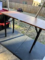 Full view of the collapsible table showing the wooden top and black folding legs in an outdoor setting.