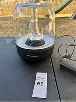 View of Harman Kardon speaker with clear dome and black fabric base, showing overall condition and design.