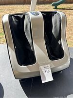 Front view of silver and black leg massager unit with fabric leg sleeves and visible Tisscare branding.