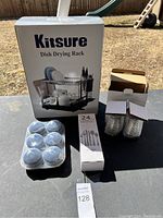 Photo showing Kitsure Dish Drying Rack box, 24-piece cutlery set box, 6 tealight candles in plastic container, and two stacked drinking glasses in box.