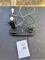 Full view of the black multi-device charging station on a table outdoors with attached power cables and a MaxSold number card.