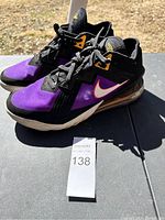 Side view of the Nike basketball shoes showing black and purple upper with white swoosh and gold accents.