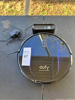 Eufy G32 Pro robot vacuum with charging dock and power adapter laid on black surface outdoors.