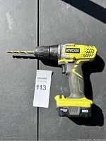 Ryobi cordless drill placed on black surface with drill bit installed and battery attached.