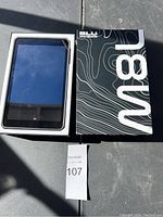 Front view of BLU M8L tablet inside its box, screen visible but reflective.