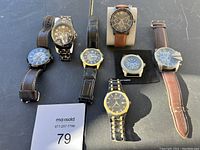 Photo showing the full collection of seven watches with various styles including leather and metal belts on black background.