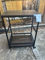 Front view of the wine cart showing the wooden top, metal frame, wheels, and bottle rack.