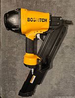 Side view of yellow and black Bostich framing nailer resting on dark surface.