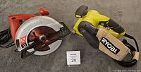Photo showing Skilsaw circular saw and Ryobi belt sander side by side on a grey surface with lot tag 28.