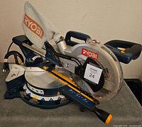 Side view of Ryobi 10-inch compound mitre saw showing dust collection bag, handle, base, and blade guard with Ryobi branding.