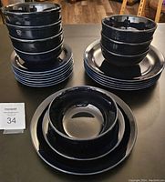 Set of black ceramic dinnerware displayed on a dark surface: stacked plates and bowls with some plates and bowls nested inside each other.