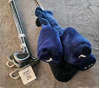 Photo of golf clubs laid flat with blue plush head covers on woods, leather grips visible, clubs arranged in order.