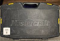 Closed Mastercraft branded black plastic case with yellow latches, showing some usage wear and scratches.