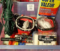 Photo of plastic bin with painting tools and supplies including painters pails, foam rollers, extension cord, sandpaper, and paint tray liners.