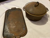 Photo showing top view of the double griddle and the Dutch oven with lid on, highlighting rust and wear on surfaces.