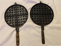 Two cast iron waffle makers with wooden handles placed side by side showing cooking surface with waffle grid.