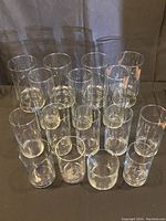 Clear cylindrical glass vases of different sizes, arranged in rows on a dark surface, all transparent glass, visible minor spots or residue.